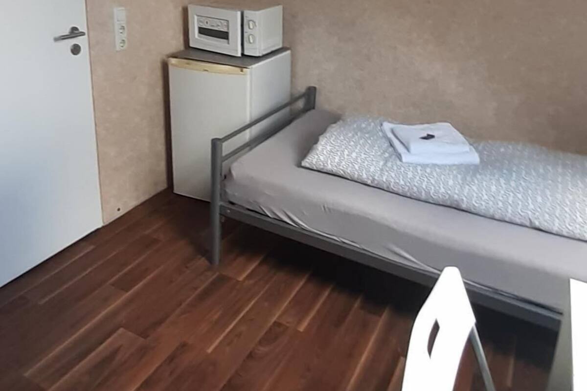 A small, compact room with a loft bed, a desk, and a microwave on a shelf.