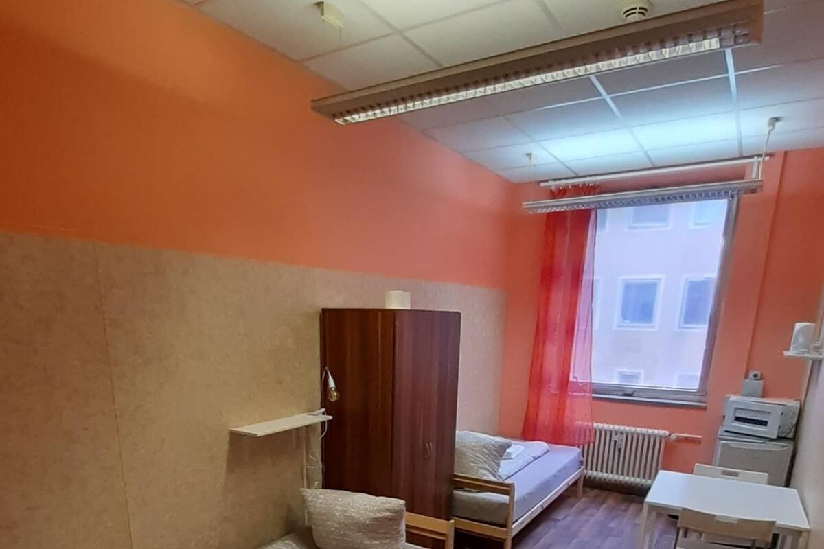 A dormitory room with a bunk bed, a single bed, a desk, and a radiator.