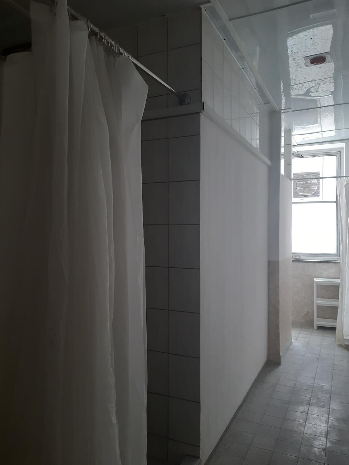 Un baño con cortina de ducha, paredes de azulejos, una ventana y un estante blanco.