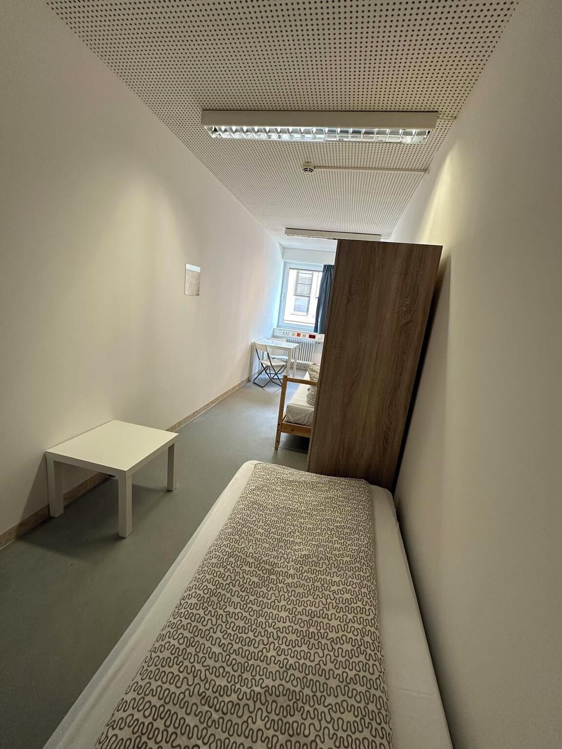 Une petite pièce comprenant un lit superposé, une petite table et une chaise.