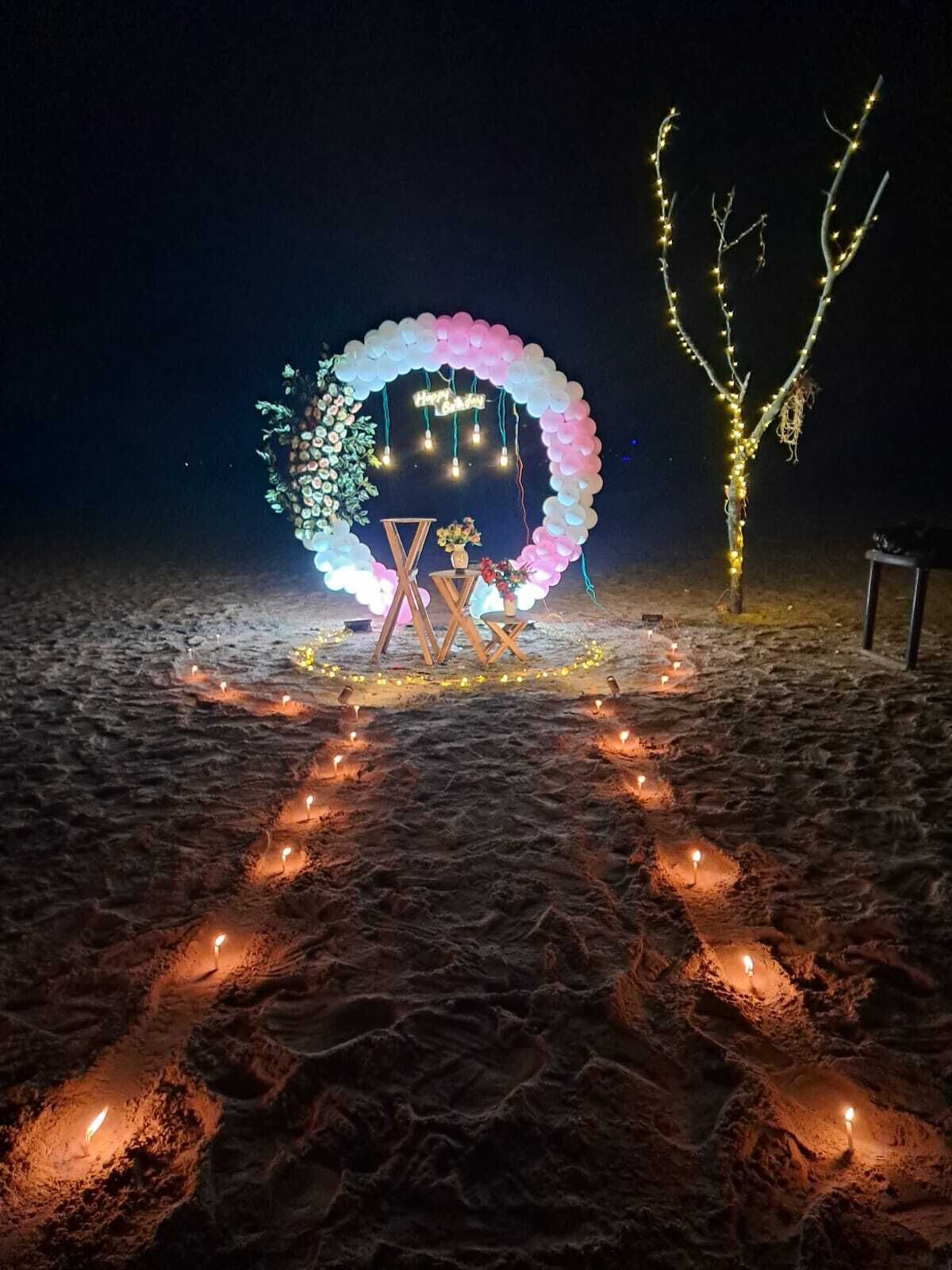Escena nocturna al aire libre con un arco decorativo y un sendero de velas iluminadas que lleva a una zona de estar.