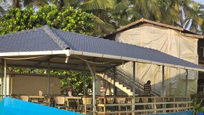 A covered outdoor seating area with tables and chairs, a staircase leading to an upper level, and a blue boat-like structure in the foreground. - Ocean Mist Beach Homestay (Bhatkal)