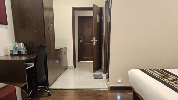 Una camera d'albergo con pavimento in legno, una scrivania con una sedia, un letto con copriletto decorato e una porta che dà su un'altra stanza.