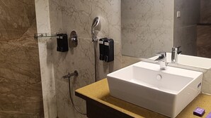 Un bagno con un lavandino bianco, uno specchio, un soffione della doccia e due erogatori di sapone.
