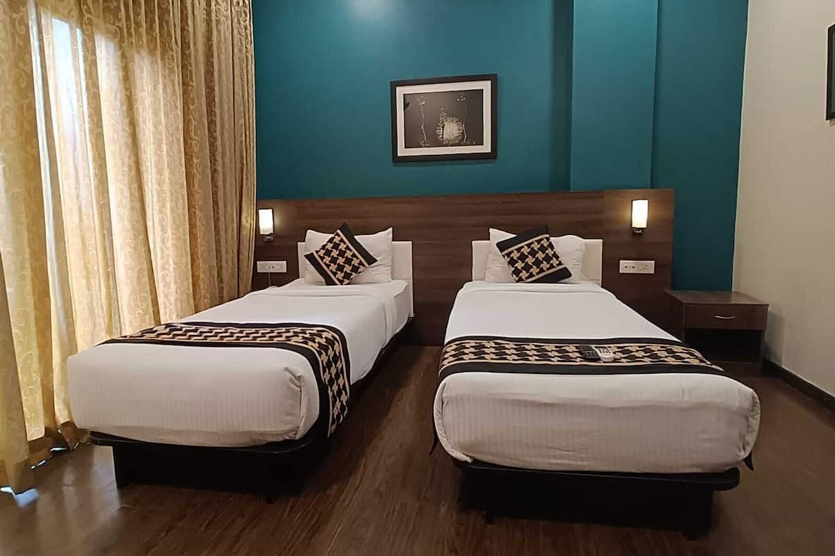 A hotel room with two beds, a wooden headboard, a framed picture on the wall, and a window with curtains.