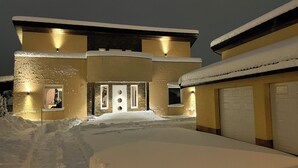 A snow-covered house with a garage, stone facade, and warm lighting. - Spacious 5-bedroom villa with beautiful panoramic view!! (Buskerud)