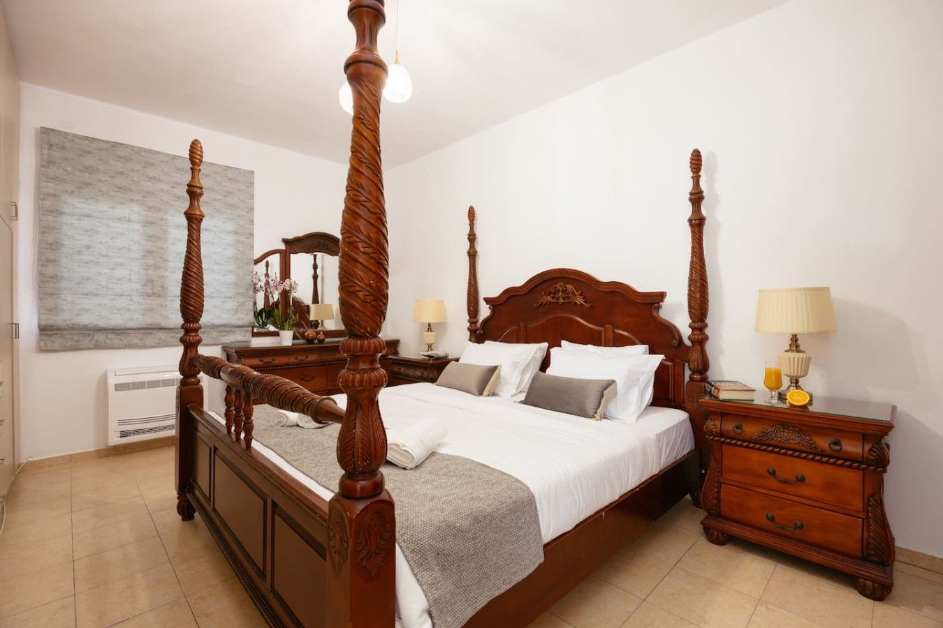A four-poster bed with a wooden headboard, a bedside table with a lamp, and a mirror on the wall.