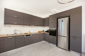 A modern kitchen with grey cabinets, stainless steel appliances, and a tiled floor. - Luxury Villa in Crete with 3 Pools, Stunning Views & Total Privacy (Argiroupoli)