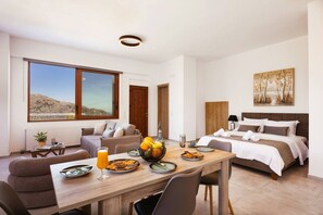 Quarto de hotel moderno com área de jantar, cama com cabeceira, janela grande com vista e uma pintura na parede.