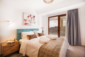 A bedroom with a bed, a nightstand, a painting, a window with a view, and a curtain. - Luxury Villa in Crete with 3 Pools, Stunning Views & Total Privacy (Argiroupoli)