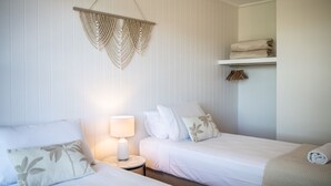 A hotel room with two beds, a hanging macrame decoration, a bedside lamp, and a shelf with folded towels. - Airlie Beach main street 2 minute walk (Airlie Beach)