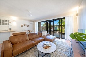 A modern living room with a leather sofa, a coffee table, and a view of the outdoors through large windows.