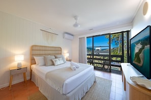 A bedroom with a large bed, a TV, and a balcony with a view.