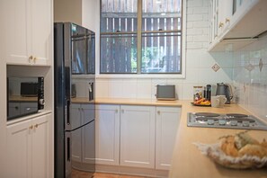 A kitchen with white cabinets, a black refrigerator, a microwave, a toaster, and a window with a view of a wooden fence.