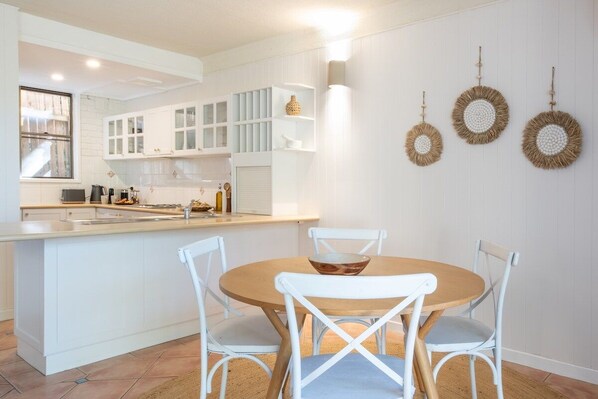 A modern kitchen with white cabinetry, a central island, and a dining area with white chairs.