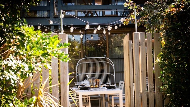 An outdoor dining area with a table set for two, surrounded by a wooden fence and string lights. - Airlie Beach main street 2 minute walk (Airlie Beach)