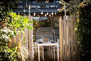 An outdoor dining area with a table and chairs, surrounded by a wooden fence and greenery.