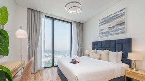 A modern hotel room with a large bed, a desk, and a view of the city through floor-to-ceiling windows. - StayShort - Stylish JBR Apartment Sleeps 4 with Marina Views (JBR)