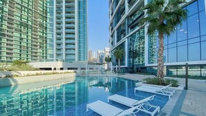 A modern hotel with a swimming pool, palm trees, and high-rise buildings in the background. - StayShort - Stylish JBR Apartment Sleeps 4 with Marina Views (JBR)