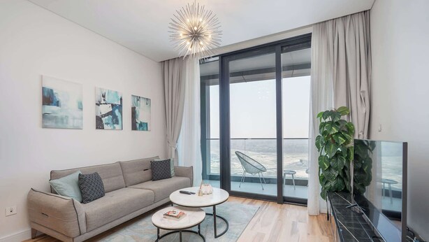 A modern living room with a sofa, two coffee tables, a TV, and a large window with a view. - StayShort - Stylish JBR Apartment Sleeps 4 with Marina Views (JBR)