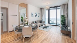 A modern living room with a dining area, large windows, and a view of the city. - StayShort - Stylish JBR Apartment Sleeps 4 with Marina Views (JBR)