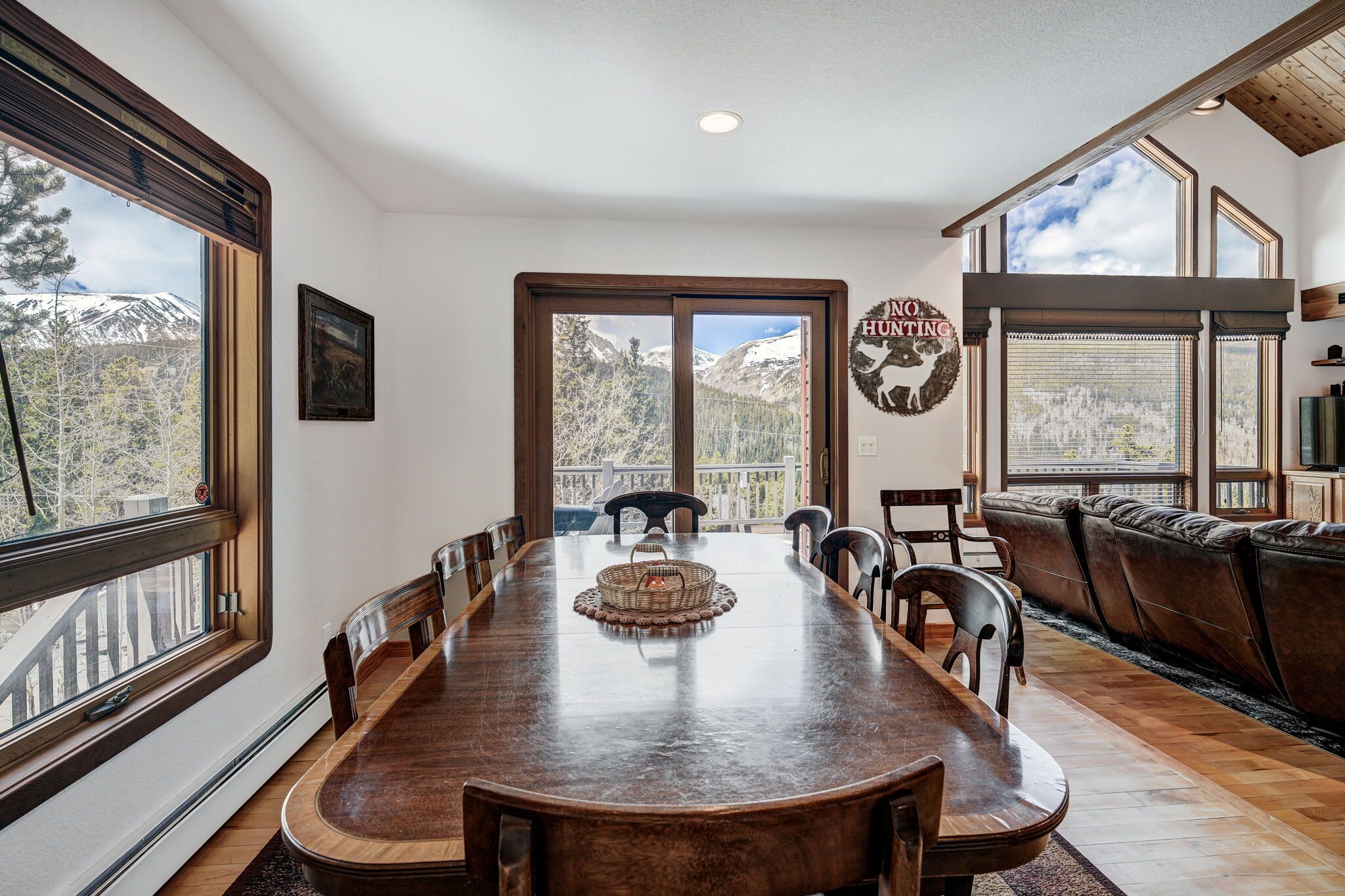 A dining area with a long wooden table, chairs, and a view of mountains through large windows.