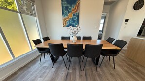 Un coin repas avec une table en bois et des chaises noires, un vase avec des fleurs blanches et un grand tableau abstrait accroché au mur.