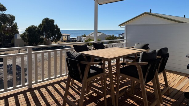 Une terrasse en bois avec une table et des chaises, donnant sur une plage et l’océan.
