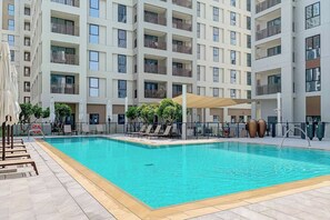 Ein modernes Apartmenthaus mit Schwimmbad, Liegestühlen und Sitzgelegenheiten im Freien.