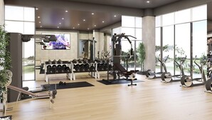 Uma academia espaçosa com diversos equipamentos de ginástica, janelas amplas e uma tela de televisão.