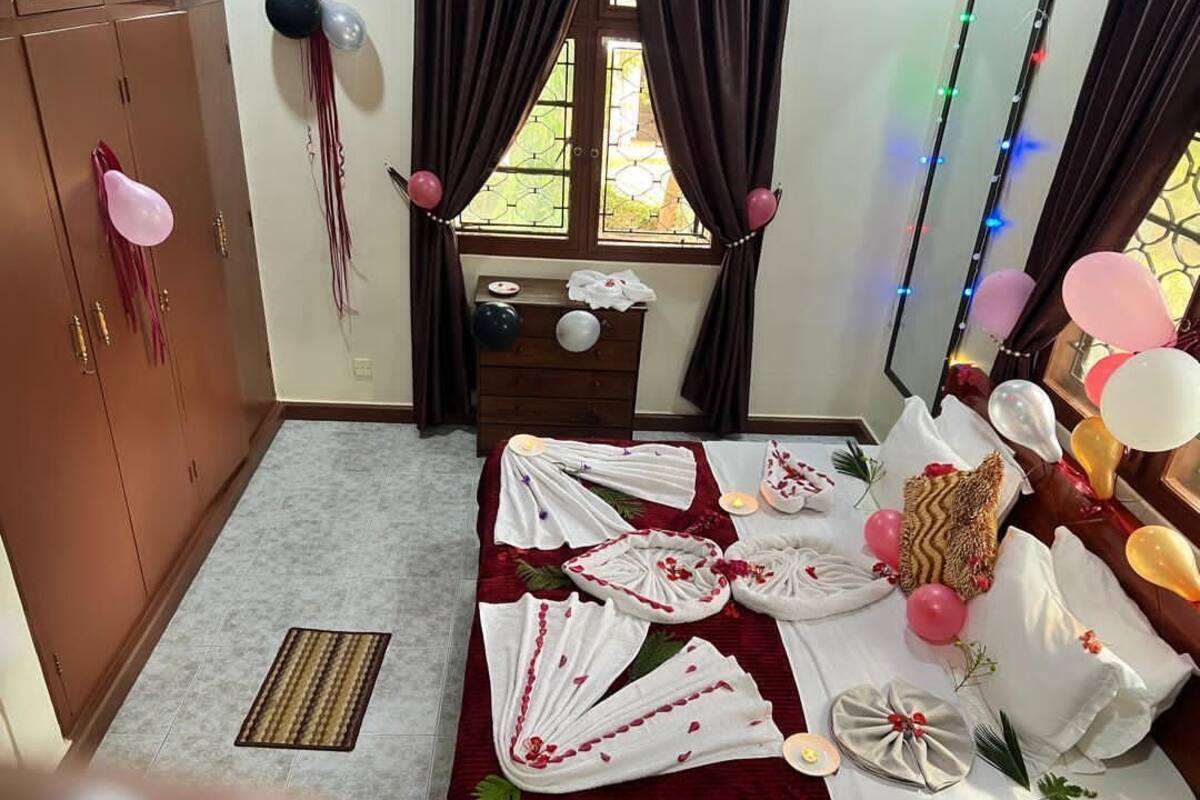 A room with a bed, a dresser, and a window with curtains. There are balloons and a table with a white cloth.
