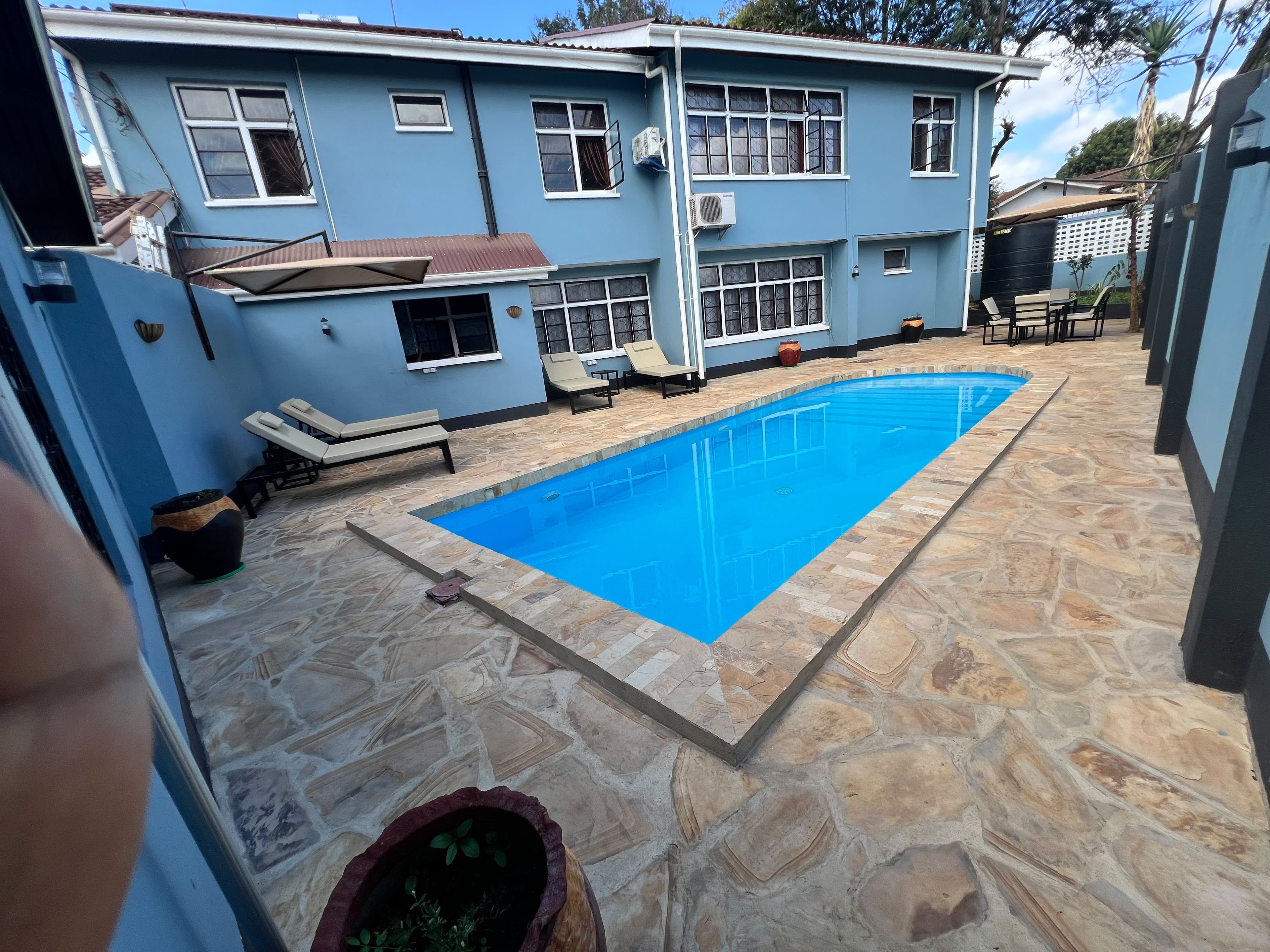 Propiedad residencial con piscina, suelo de piedra y una casa azul.