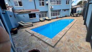 Propiedad residencial con piscina, suelo de piedra y una casa azul.