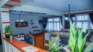 Un espace d’accueil avec un comptoir en bois, des plantes en pot, un téléviseur et une fenêtre avec des rideaux.
