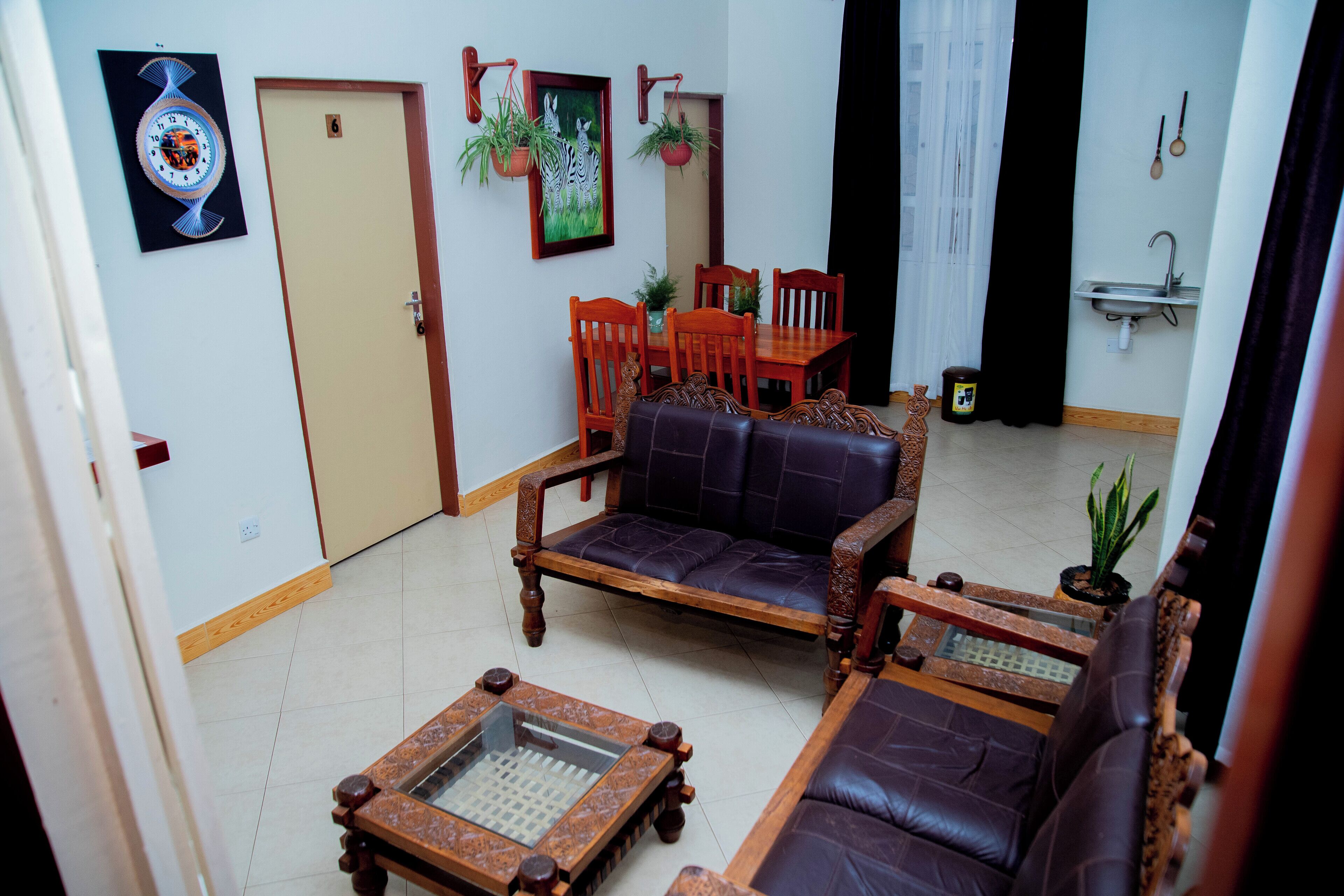 Una sala de estar con sofá, sillones, una mesa de centro, una mesa de comedor con sillas, un reloj en la pared y una planta en maceta.