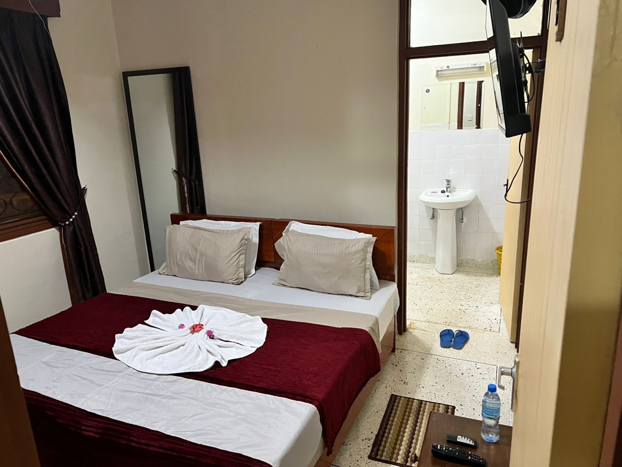 A hotel room with two beds, a mirror, a sink, and a TV.