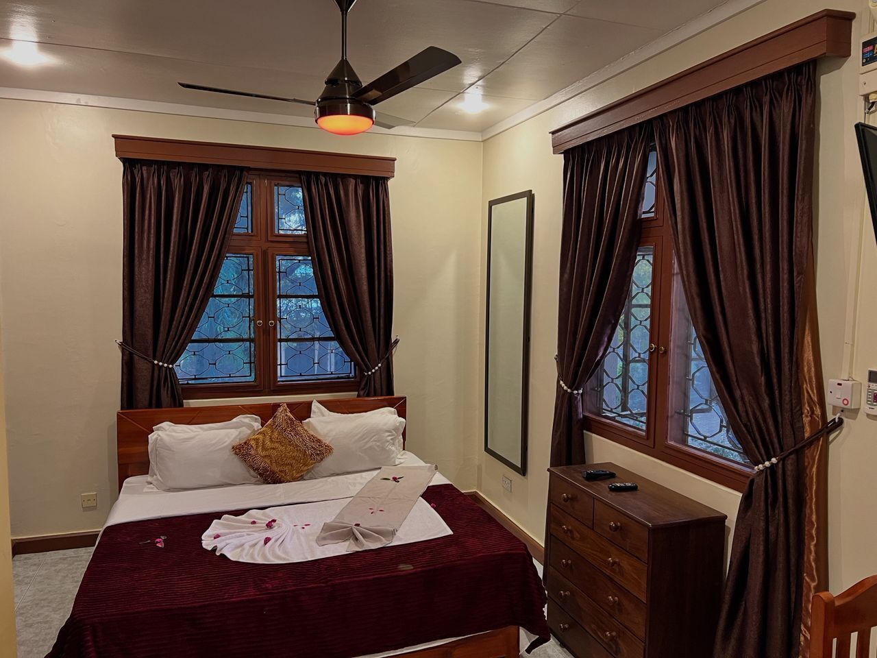 A bedroom with a bed, a dresser, a mirror, and a ceiling fan.