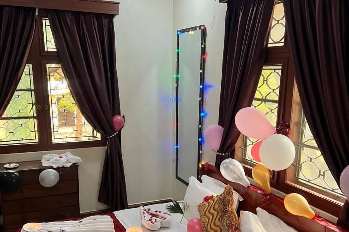 A well-lit bedroom with a bed, curtains, a mirror, and a window with a view.