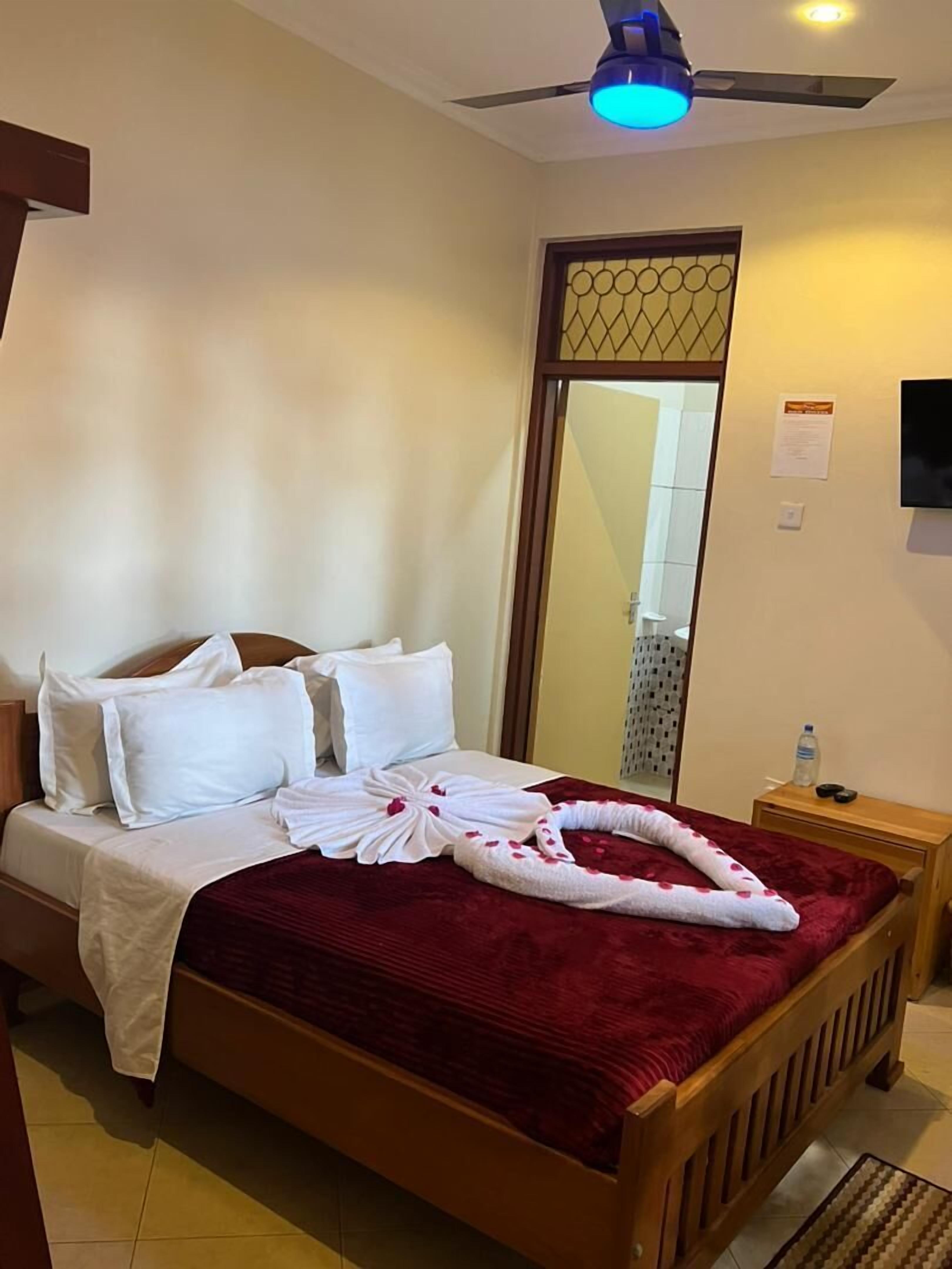 Une chambre d’hôtel avec un lit, une table de chevet en bois, un ventilateur de plafond et un miroir.