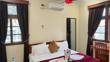 A hotel room with a bed, a ceiling fan, an air conditioner, a water bottle, and a window with curtains.