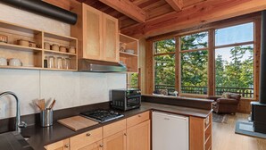 A modern kitchen with wooden cabinets, a black countertop, and a view of the outdoors through large windows.