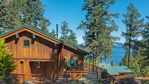 A wooden cabin with a deck, surrounded by trees and a lake view.