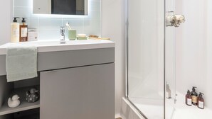 A modern bathroom with a glass shower enclosure, a vanity with a mirror, and a built-in shelf with toiletries.