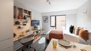 A modern hotel room with a desk, chair, and a bed with a view of the outside.