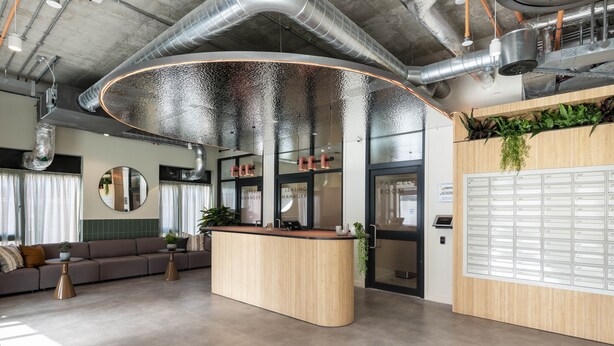 A modern reception area with a curved wooden counter, a seating area with a sofa and coffee table, and a plant wall.