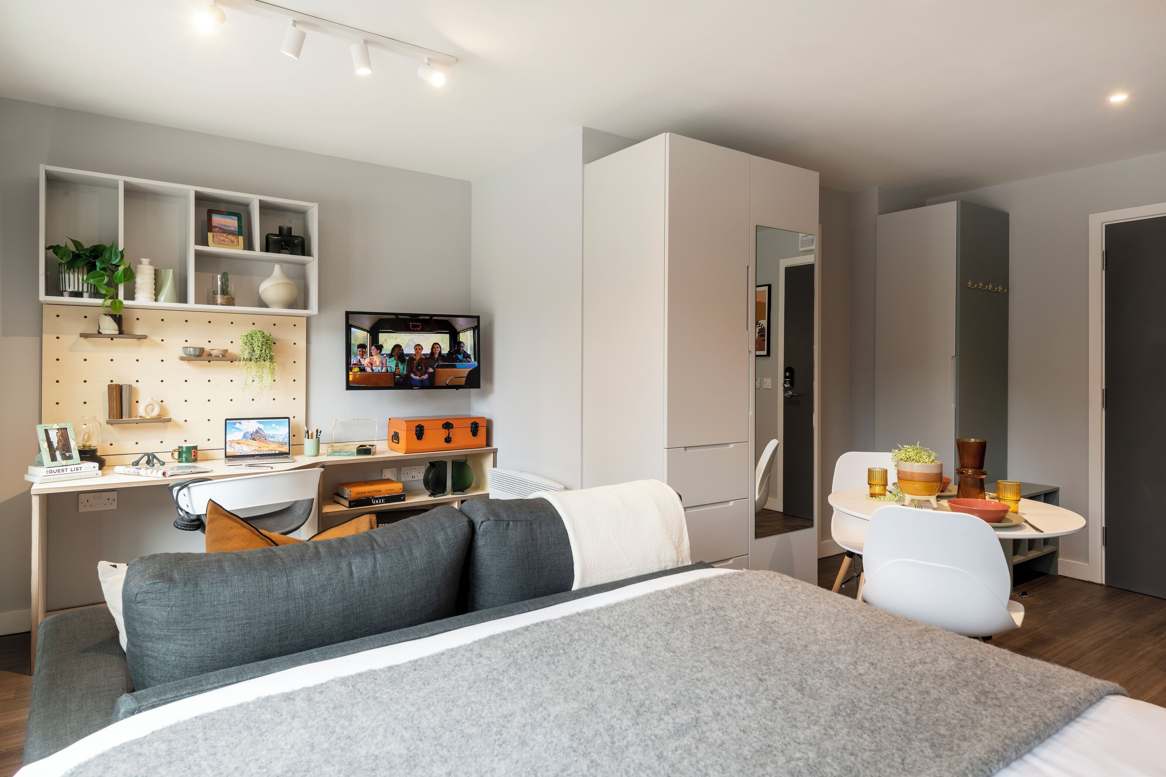 Una habitación de hotel moderna con una cama, un escritorio con computadora, un televisor y un área de comedor.