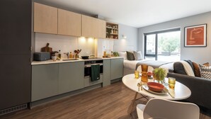 A modern kitchen with grey cabinets, a dining area with a white table, and a sofa with cushions.