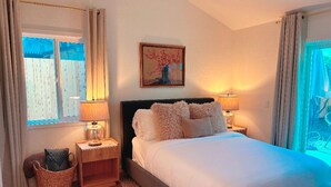 Une chambre avec un grand lit, deux tables de chevet avec des lampes, une petite table en bois, un panier en osier et un tableau accroché au mur.