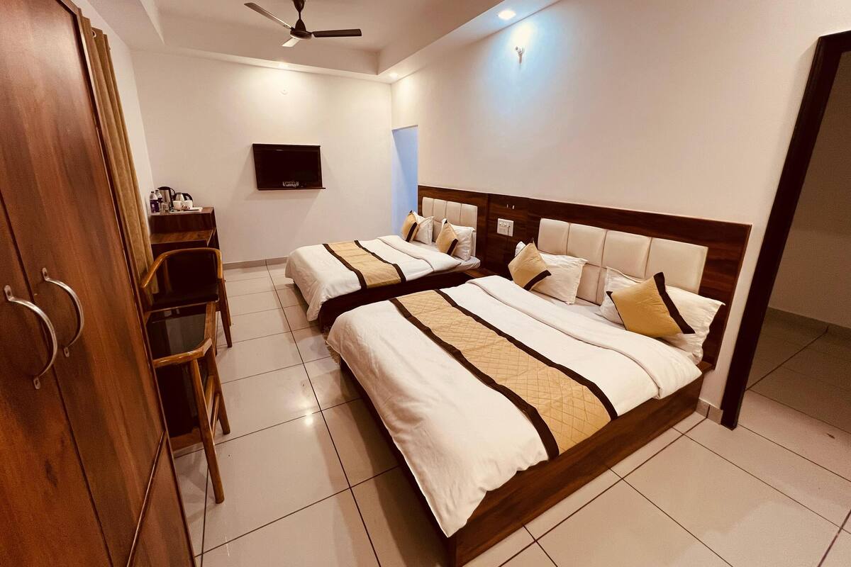 Habitación de hotel con dos camas, un escritorio, una silla, un televisor y un ventilador de techo.