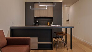 Ett modernt kök med en mörk bänkskiva, en kaffemaskin och en barstol.